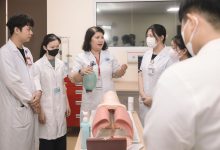 Grupo de estudantes de medicina pratica procedimentos com um manequim de treinamento em uma sala de aula.
