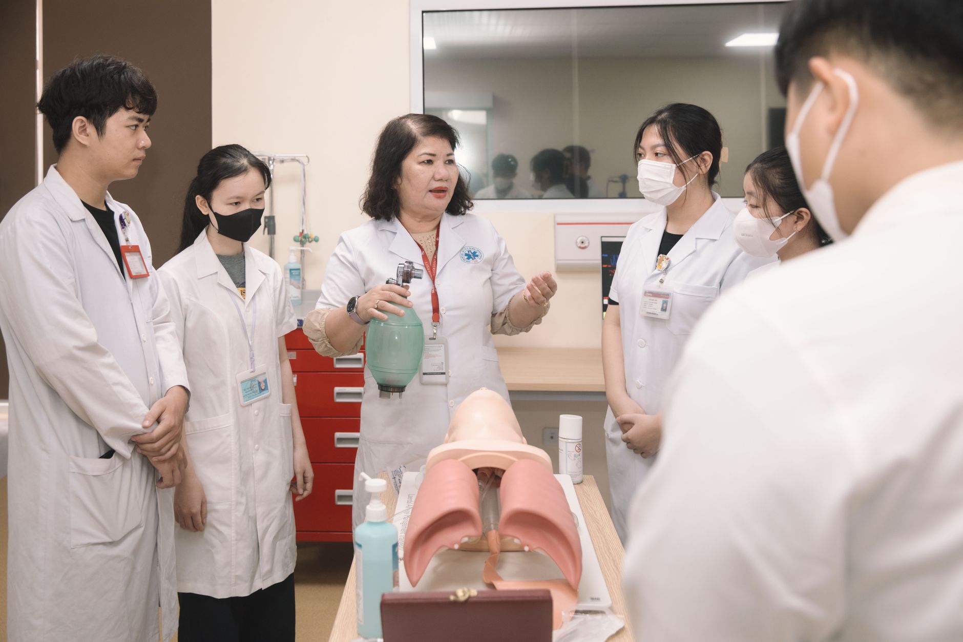 Grupo de estudantes de medicina pratica procedimentos com um manequim de treinamento em uma sala de aula.
