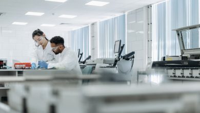 Dois pesquisadores trabalham em um laboratório de alta tecnologia usando óculos de proteção e luvas.
