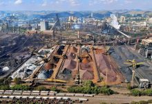 Vista aérea de uma ampla instalação de mineração no Brasil, com máquinas industriais e pilhas de rejeitos.