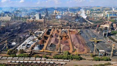 Vista aérea de uma ampla instalação de mineração no Brasil, com máquinas industriais e pilhas de rejeitos.