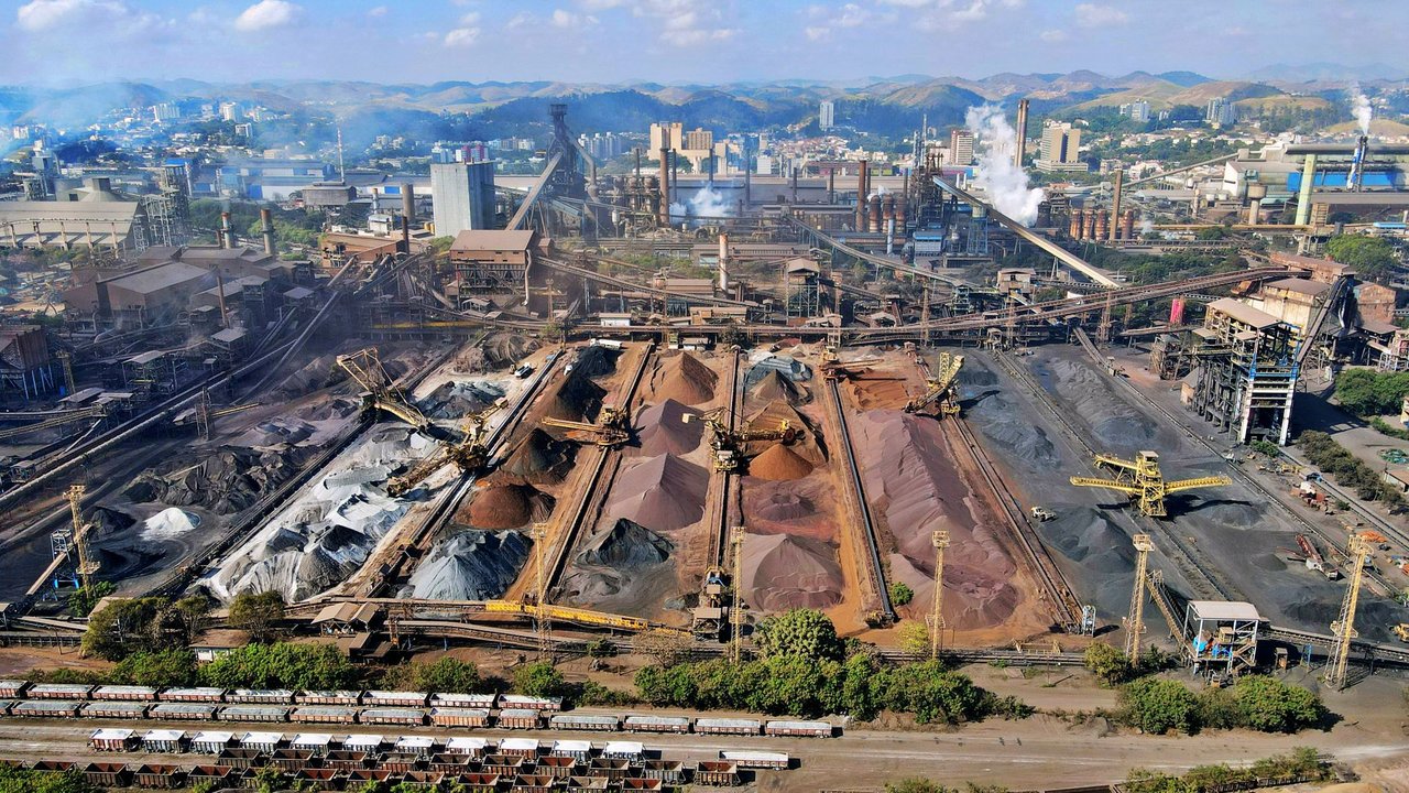 Vista aérea de uma ampla instalação de mineração no Brasil, com máquinas industriais e pilhas de rejeitos.