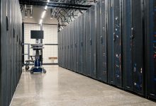 Fileiras de gabinetes metálicos com servidores, equipamentos de rede e cabos em um data center moderno.