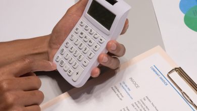 Mãos usando uma calculadora ao lado de uma fatura e documentos financeiros sobre uma mesa.