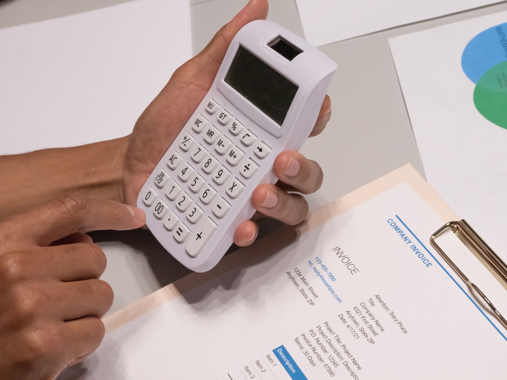 Mãos usando uma calculadora ao lado de uma fatura e documentos financeiros sobre uma mesa.
