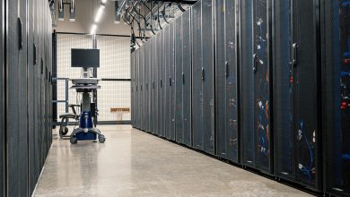 Fileiras de gabinetes metálicos com servidores, equipamentos de rede e cabos em um data center moderno.