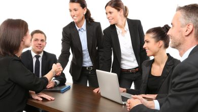 Grupo de pessoas reunido em um escritório, em uma conversa de trabalho, com participantes cumprimentando-se à mesa.