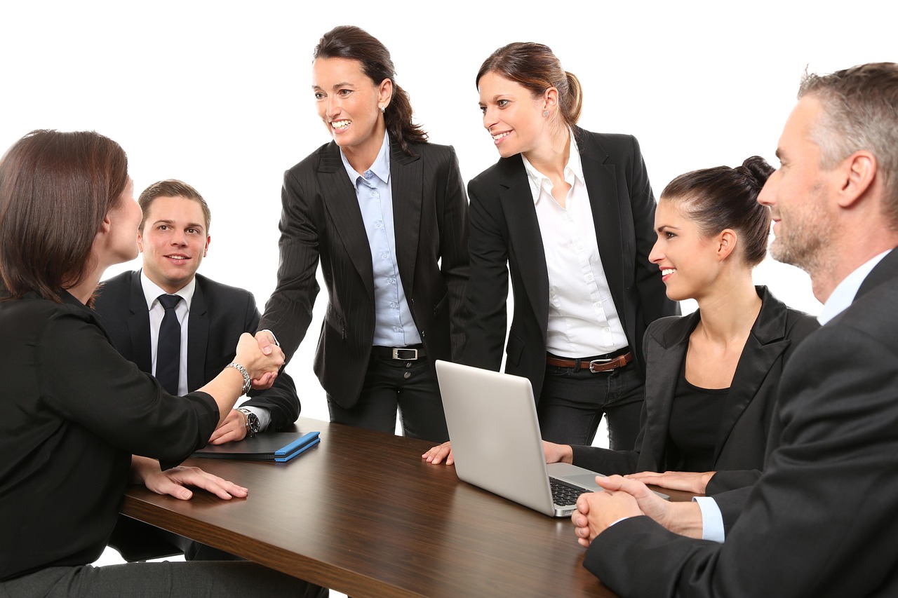 Grupo de pessoas reunido em um escritório, em uma conversa de trabalho, com participantes cumprimentando-se à mesa.